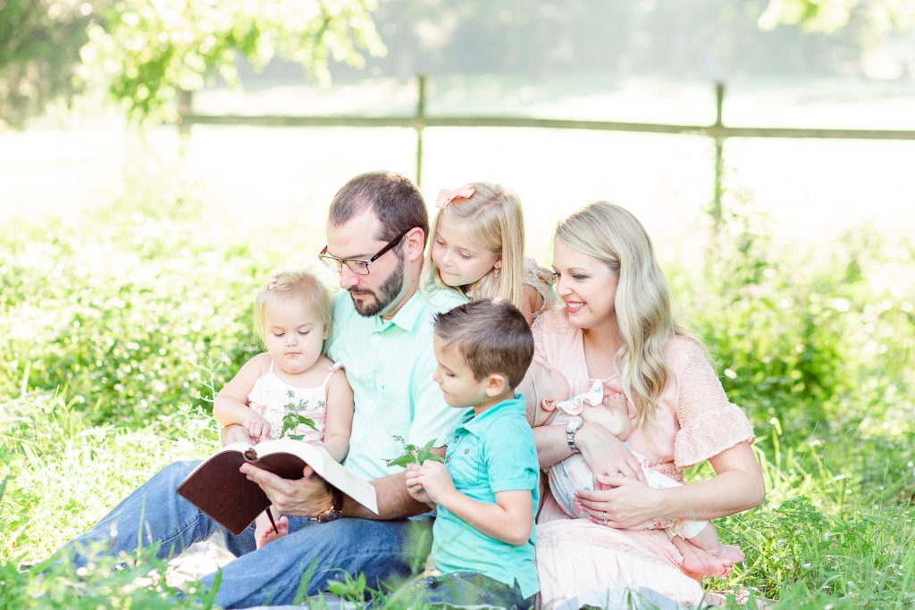 Family Photo of the Brazzells sitting in the grass with a fence in the background. They are sitting in grass. This image is used in the logo of the No Higher Calling Podcast.