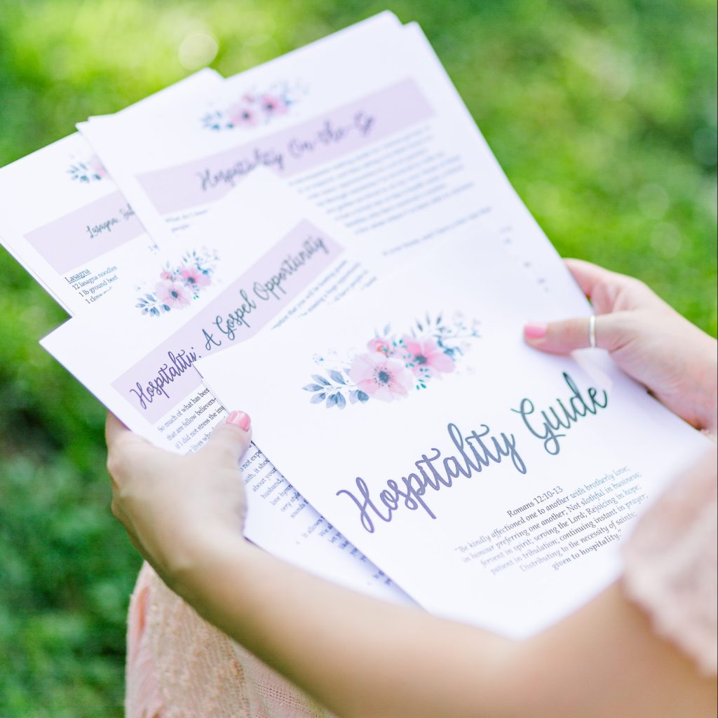 The Hospitality Guide spread out on a woman's lap. There is grass in the background out of focus. The woman is in a peach dress.