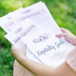 The Hospitality Guide spread out on a woman's lap. There is grass in the background out of focus. The woman is in a peach dress.