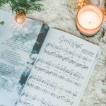 Great Hymns for Growing Hearts - Christmas Edition. The book is open to show the music to "Silent Night." It is laying on a furry, white rug with a candle and evergreens around it.