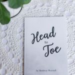 Head to Toe Prayer Journal. The white edition of the book is laying on a white tablecloth with a green plant next to it.