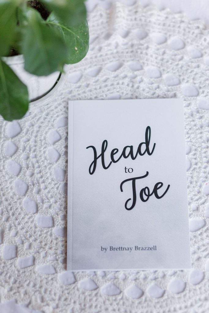 Head to Toe Prayer Journal. The white edition of the book is laying on a white tablecloth with a green plant next to it.