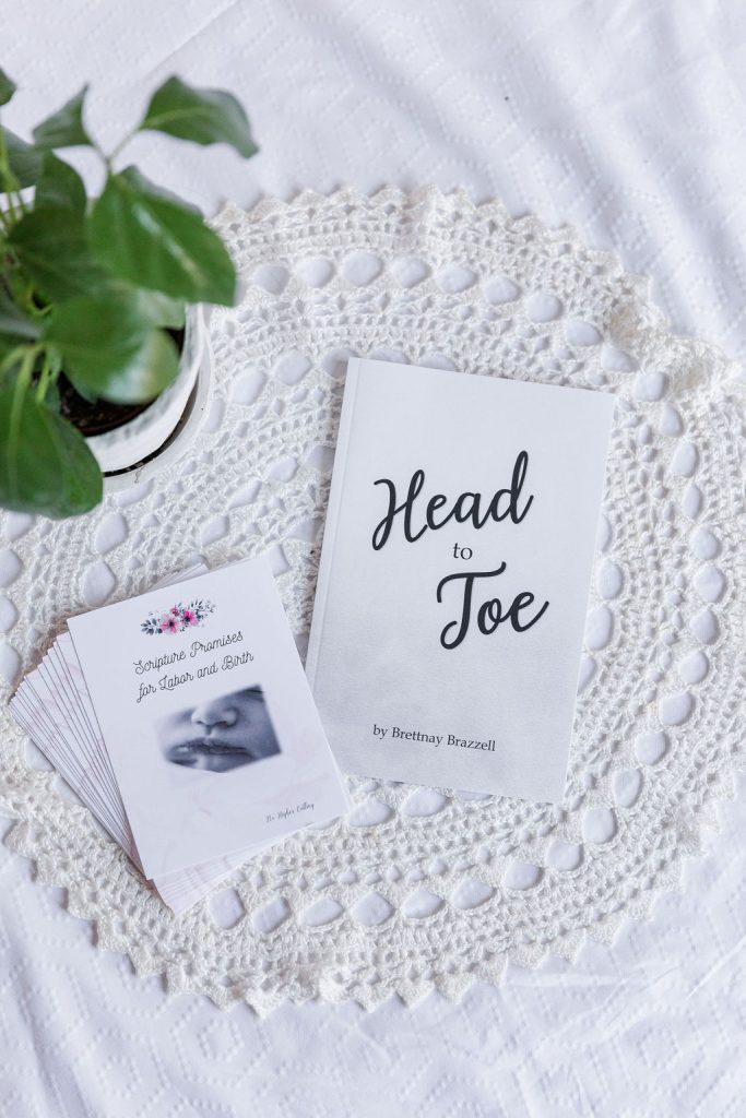 A white Head-to-Toe Prayer journal and the "Scripture Promises for Labor and Birth" cards laying on a white blanket with a green plant next to them.