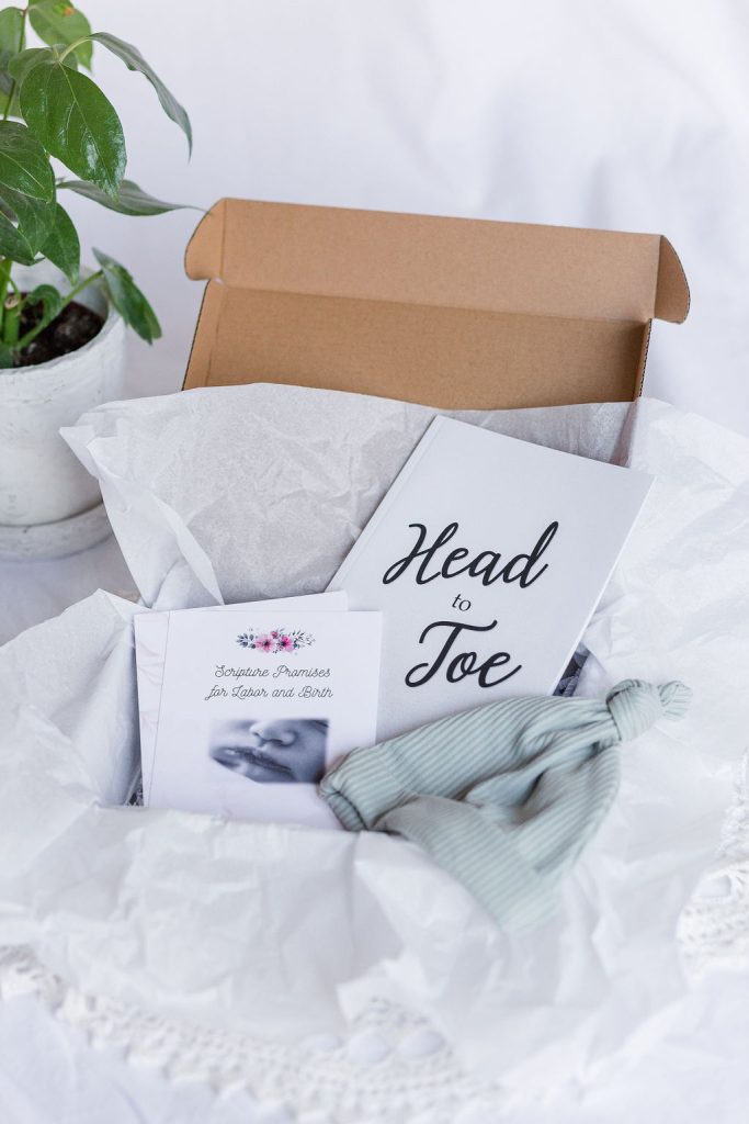 A close up of the white set. It contains a Head-to-Toe Prayer Journal, a Scripture Promises Labor and Birth Card set, and a baby hat