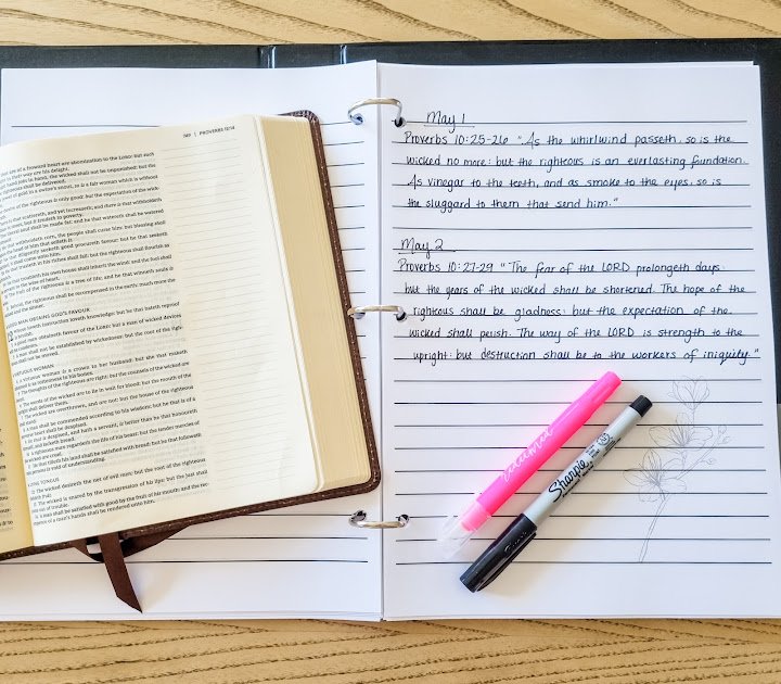 Open notebook with scripture written under daily headings shown with an open Bible, a highlighter, and a pen