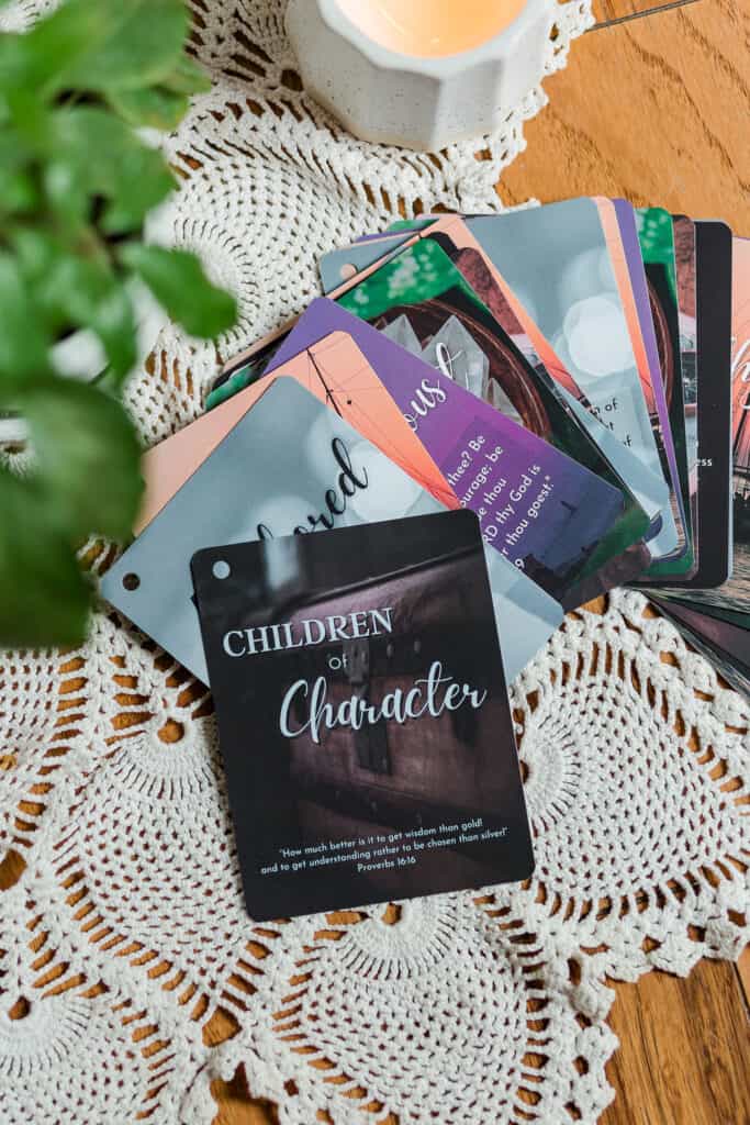 The Children of Character Cards with the ring removed and spread out on a table. The cards are several colors and have various background images. The table has the cards, a plant, and a candle on it.