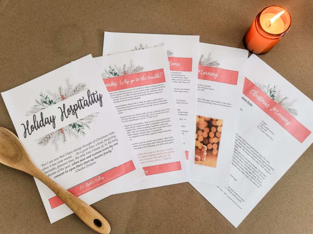 The Holiday Hospitality Guide laying out on a brown floor. There are a few images and parts of recipes that can be seen. There is a wooden spoon and a candle next to it.