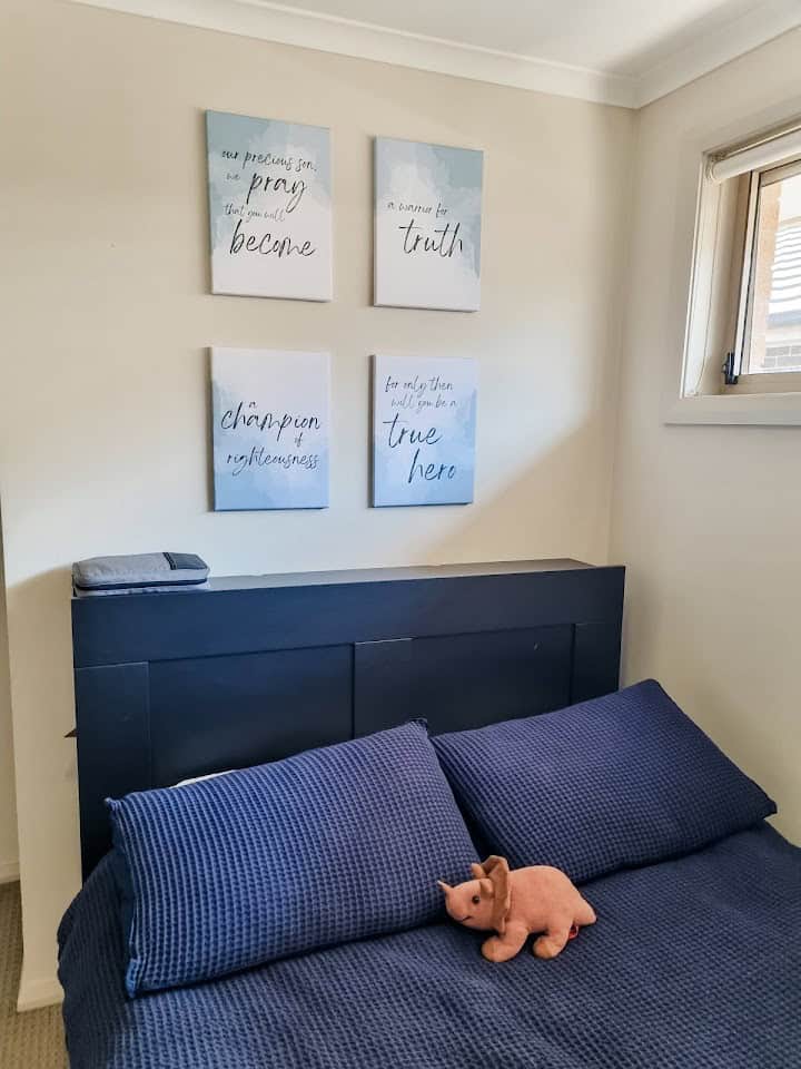 The "Warrior for Truth: Printable wall art" printed on canvases and hanged over the top of a bed. On the bed are blue covers and pillows as well as a stuffed dinosaur.