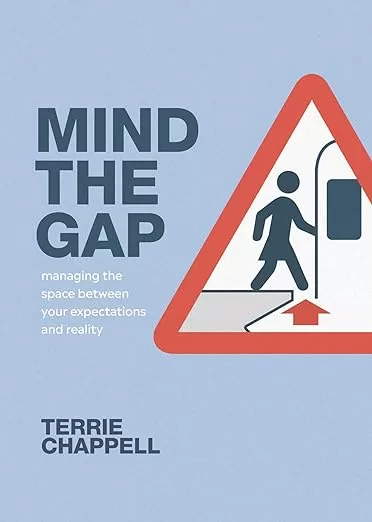 Book Cover for "Mind the Gap" by Terrie Chappell. It has a blue background and has a "mind the gap" caution sign showing a woman stepping over the gap and getting on a train.