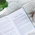 Great Hymns for Growing Hearts Interior Image showing the music to the hymn along side the story behind the hymn. The book sits on a table with hot chocolate and a plant.