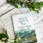 Great Hymns for Growing Hearts book laying on a table with flowers around it. On the table is a hymn book laying open as well.
