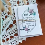 A stack of Friendship Cards wrapped in twin with a bow. It is sitting on a hardwood table covered in lace along side a few pens.