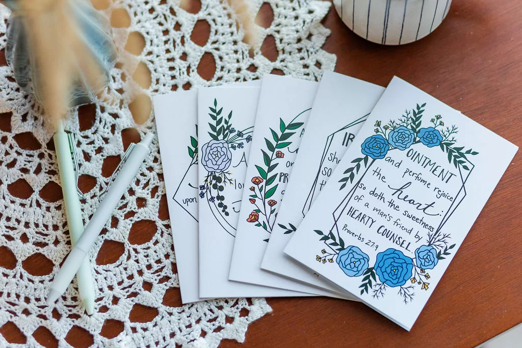 Five Friendship Cards flayed out on a wooden table that is covered in lace with 2 pens beside them.