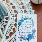 A Friendship card laying on a wooden table with a lace cover. The card reads "Ointment and perfume rejoice the heart: so doth the sweetness of a man's friend by hearty counsel." Proverbs 27:9