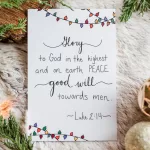 A single Christmas card laying on white fir and surrounded by greenery. It reads "Glory to God in the highest, and on earth Peace, good will towards men." Luke 2:14