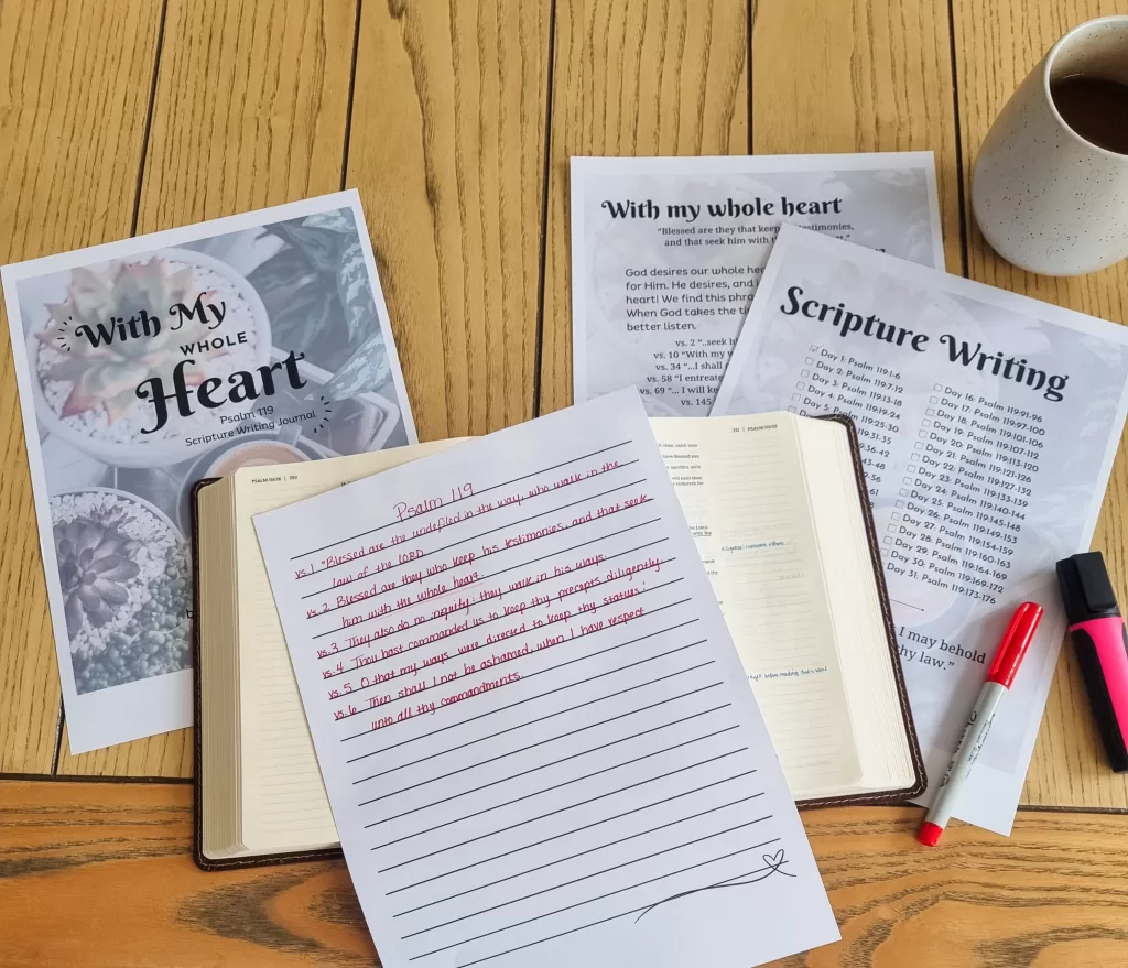 The Psalm 119 writing plan beneath a bible and a written on notepage along side a red pen. They are all sitting on a wooden table.