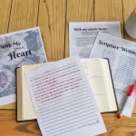The Psalm 119 writing plan beneath a bible and a written on notepage along side a red pen. They are all sitting on a wooden table.